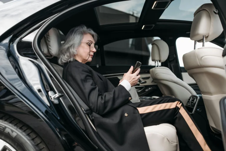 Senior businesswoman sitting in luxury car using a smartphone